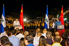 Nayib Bukele and standing at podiums in front of Chinese and Salvadoran flags with a construction crew in the background