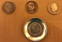 Three coppery coins grouped with a silver one, the last mounted in a dish. They are all Kalākaua dollars by design.