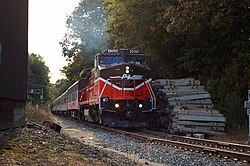 A diesel locomotive pulling a passenger train down a railroad track, heading towards the observer. The locomotive has P&W's logo on its nose, and is numbered 4006. A pile of concrete railroad ties lies next to the track.