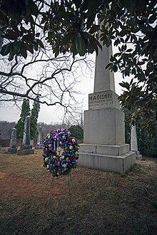 James Madisons Grabmal, eine mehrere Meter hohe Säule, aus Froschperspektive. Davor steht ein Blumenkranz.