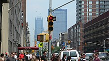 A busy daytime street scene, with both the bike signal and pedestrian signal glowing red. People and cars are everywhere. Many other traffic signals can be seen in the background as you look further down the street.