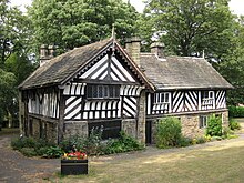 Photograph showing a timber-framed house. There are two sections to the building at right angles to each other forming a T shape. The ground level of the building has stone walls, whereas the upper floor has wattle and daub infill.