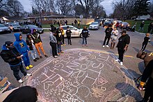 A vigil for Wright near where he was killed. People standing around a circle on the ground where messages remembering Wright and calling for justice have been written in chalk.