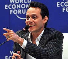 A man sitting next to a microphone is pointing to the right.