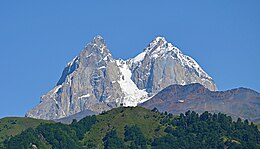 A double-peaked, snow-covered mountain under cloudless blue sky