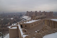 A stone fortress in a city, recently snowed upon.