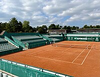 A clay tennis court with spectator seats around it