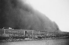 A large cloud of dust next to a farm