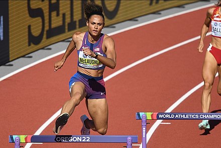 Sydney McLaughlin seen from the front, wearing a purple kit while jumping over a hurdle