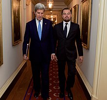 A photograph of John Kerry (left) and Leonardo DiCaprio both dressed in suits and looking away from the camera