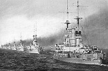 Several large light gray warships steaming in a line, closely together; thick smoke pours from all of their smoke stacks.