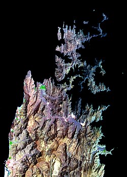 The peninsula as seen from space. Al-Khasab to the north (top) shown in green, is contrasted between the more subtle rainbow tones of the surrounding rock in this false-colour image. The term Khasab refers to the fertility of the soil.