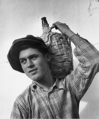 Man carrying a jug with woven wicker handle. Portugal, 1950
