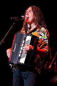 Yankovic holding an accordion whilst singing into a microphone.