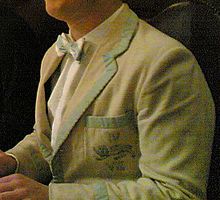 Photograph of a young man wearing a cream jacket with Cambridge blue trim. On the breast pocket, embroidered in Cambridge Blue thread, are a lion and the Roman numerals IV and VIII