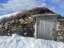 A wooden door, set into a stone frame, partially covered by snow