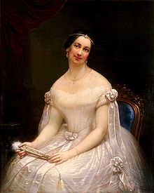 Julia Tyler sits for a portrait and smiles. She has dark hair and is dressed in a fancy white gown, holding a matching white feathered fan in her hands.