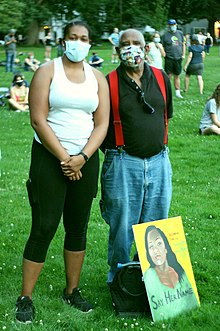 A young woman and an older man pose for a picture in a field among a socially distanced crowd.