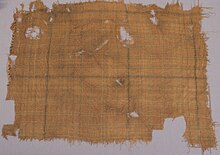 A faded and somewhat tattered span of tartan cloth, presently looking tan with various dark lines across it