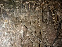 Amun accompanied by Mut with the uraeus-pinnacle shown crowned with a sun disk hanging from the cliff.