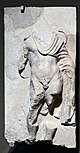 A marble relief of a man wearing a toga; the head is missing, along with parts of all four limbs