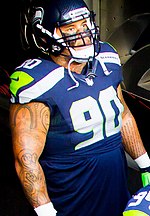 A picture of Jesse Williams in American football gear, showing their tattoos.