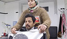woman wearing a headscarf prepares to cut a man's hair