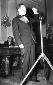 A photograph showing Long raise his fist as he speaks into a microphone