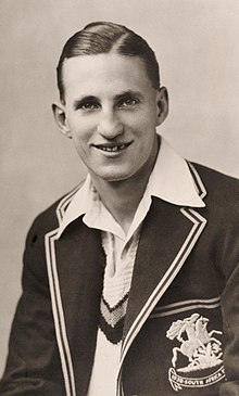 A black and white photograph of a young man wearing cricket whites and a blazer