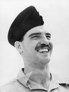 Informal head-and-shoulders portrait of grinning moustachioed man in forage cap