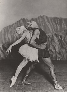 Two dancers pose in front of a rocky background