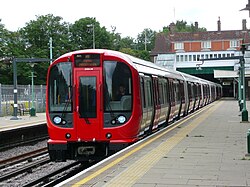 A grey, blue and red S8 stock train waiting at the platform at Croxley station