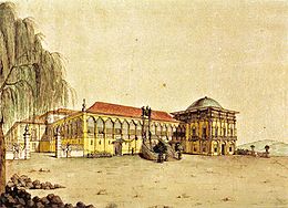 Colored lithograph showing the facade of the palace with gateway on the left leading to the side of the complex. In the center of the front, a central double staircase leads up to a doorway on the galleried main floor which is surmounted by the Imperial arms, while a large domed, square tower rises on the right side of the building.