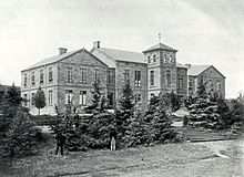 A black and white photograph of a large mansion house, surrounded by various trees