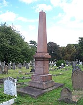 A tall red four-sided obelisk, surrounded by much shorter gravestones