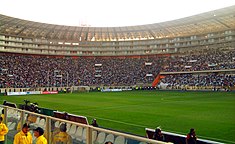 Photograph of a modern football stadium's interior; the stands are full of spectators