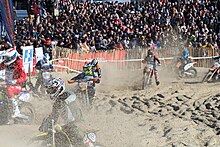 Bikers race past spectators in sand