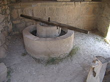 A reconstructed olive press from Volubilis consisting of a circular stone basin with a circular stone inset, atop which a long wooden bar is fixed