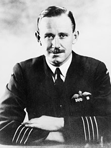 Half-length portrait of moustachioed man in military uniform, with aviator's wings on left breast pocket and four stripes on jacket forearms