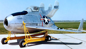 Small potato-shaped aircraft with three vertical stabilizers, resting on yellow movable rig