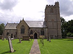 Stone church with square tower. In the foreground are a path and gravestones