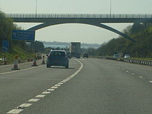 multi-carriageway road with vehicles passing under an elevated roadway and distant view of sea beyond