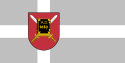 Silbergrau-weiße Kreuzflagge der Stadt Alūksne im Nordosten Lettlands mit dem Stadtwappen in der Mitte[46]