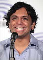 A 45-year-old man is shown in a head shot. He is broadly smiling and is in front of a microphone.