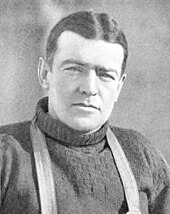 Head and shoulders of a dark-haired man looking directly to camers. The straps of a harness over his shoulders are visible.