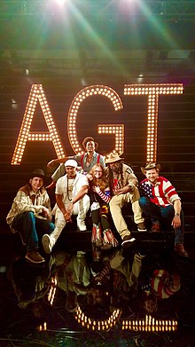 Rench the Mastermind (guitar, beats, vocals), Dolio the Sleuth (MC, vocals), B.E. Farrow (fiddle, vocals), Sleevs (manager), R-SON the Voice of Reason (MC), Dan "Danjo" Whitener (banjo, vocals), all seated in front of AGT sign.