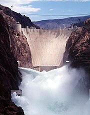 Front view of a dam in a narrow canyon, with water shooting out of the gates