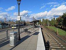 Photograph showing the WES Commuter Rail platform with tracks on the right and several buses on the at a platform on the left