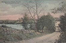 Hand-colored postcard depicting a road bordered by a stone wall next to a pond. Text in the upper left-hand corner reads "Windham Frog Pond, Windham, Conn."