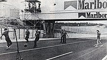 Black-and-white photograph of men playing football on a racetrack